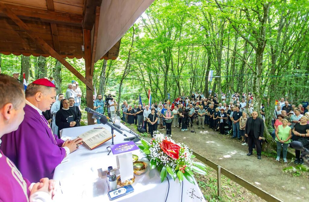 Misa na otvorenom uz veliko okupljanje građana i svećenika u šumovitom području, uz cvijeće i lampione na oltaru.