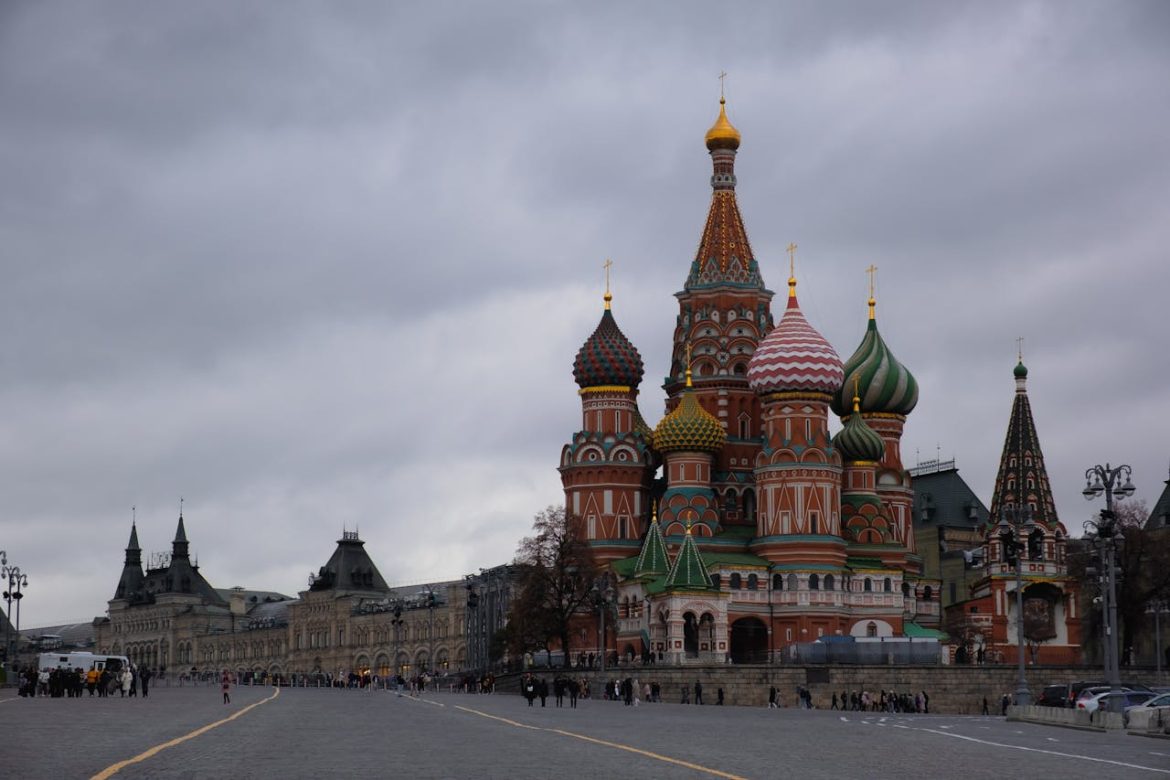 Saint Basil's Cathedral with its colorful onion domes on Red Square under a cloudy sky, with people strolling in the foreground.