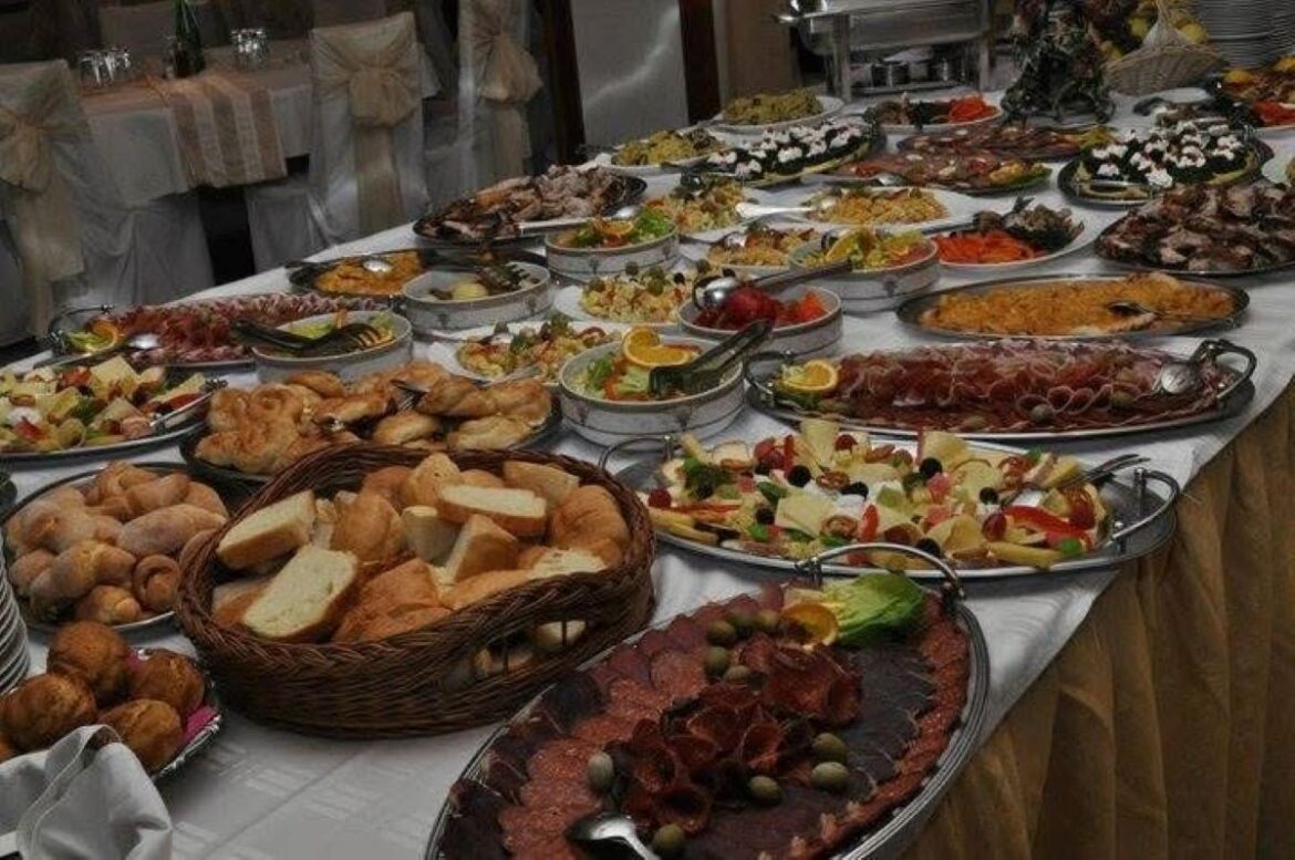 Lavish buffet spread on a long table with breads, cheeses, meats, salads, and other dishes for a formal reception.